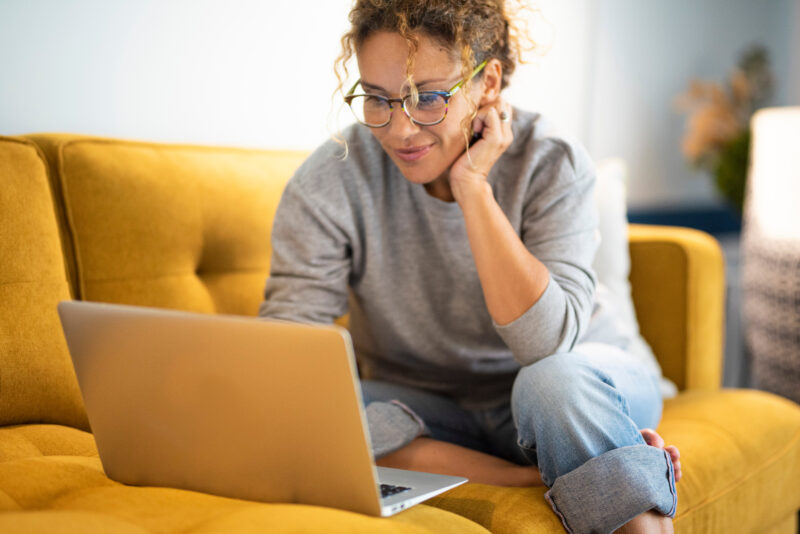 Eine Frau sitzt mit dem Laptop am Sofa