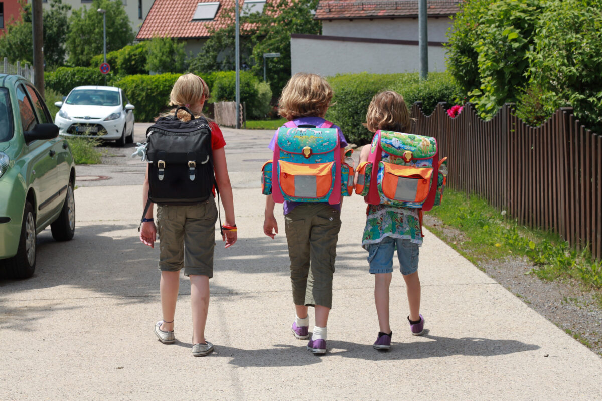 Drei Kinder mit Schultaschen gehen eine Straße entlang
