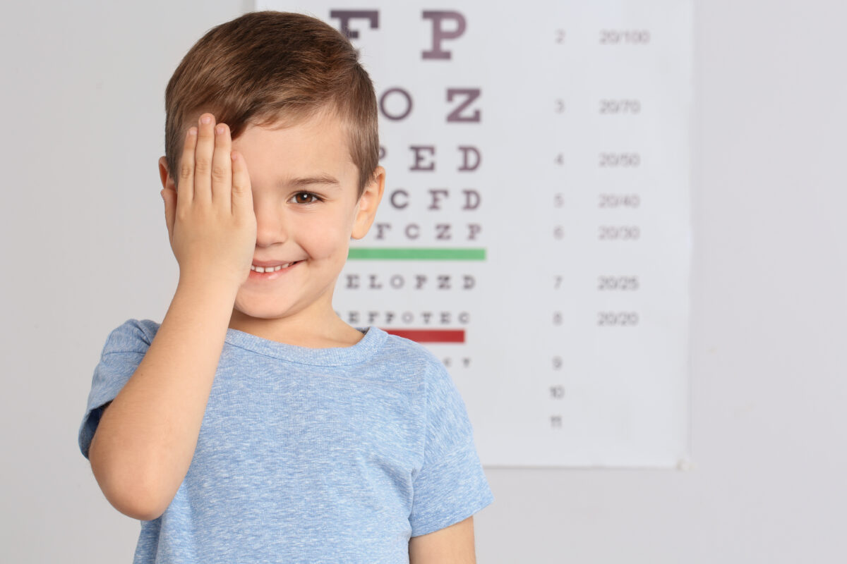 Kleiner Junge hält sich mit der rechten Hand das rechte Auge bei einem Sehtest zu