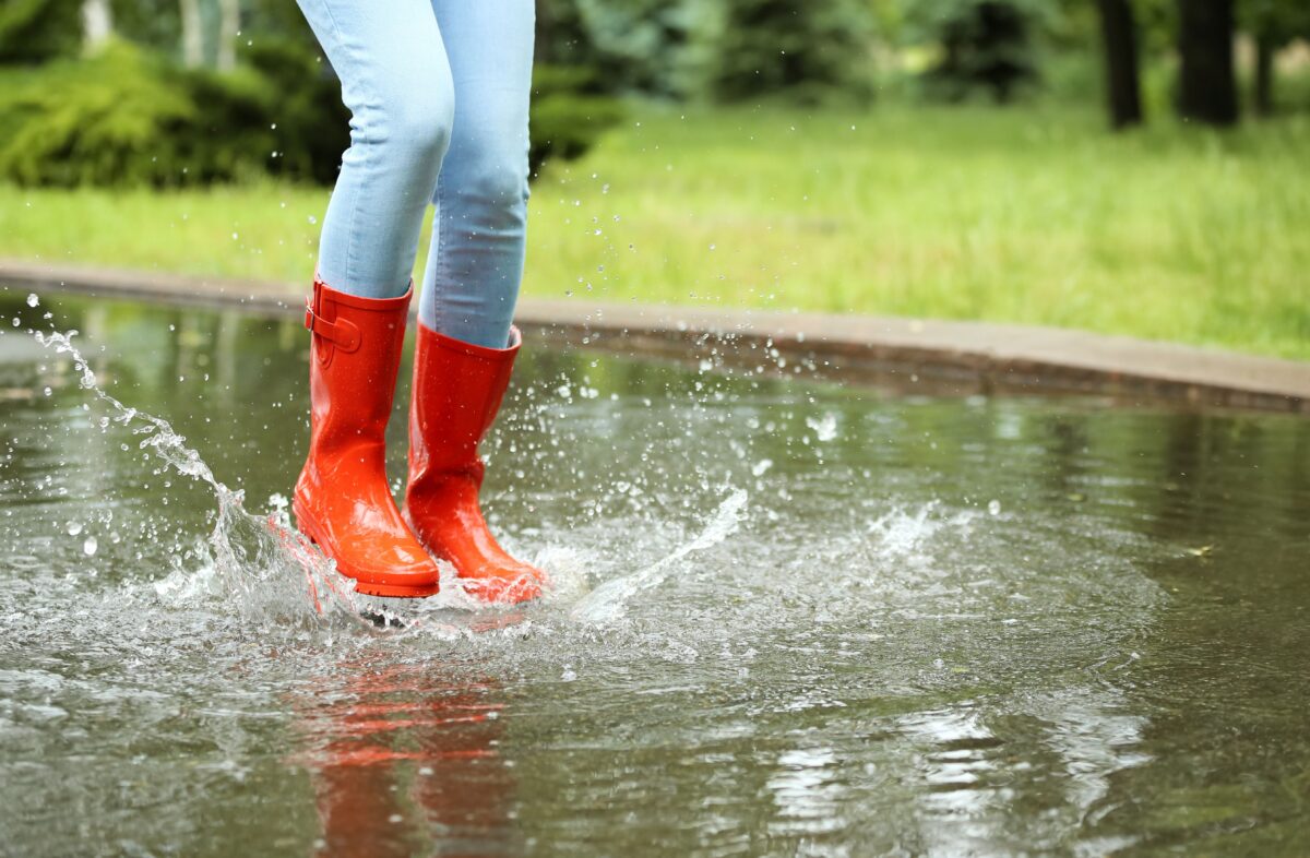 Person mit roten Gummistiefeln springt in Pfütze
