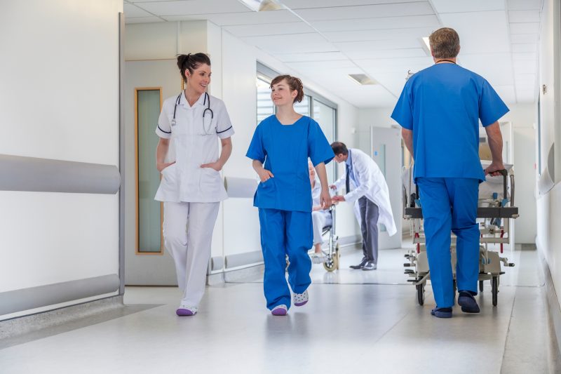 Ärztin, Arzt, Pflegepersonen und Patientin im Rollstuhl in einem Krankenhausgang